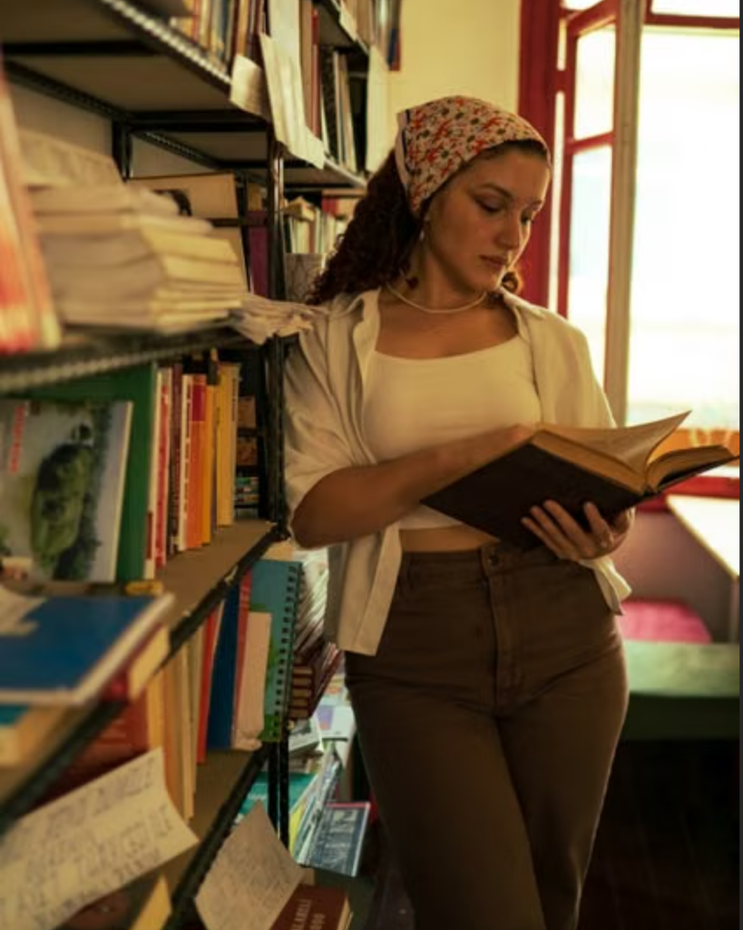 Woman reading a book between tall library shelves