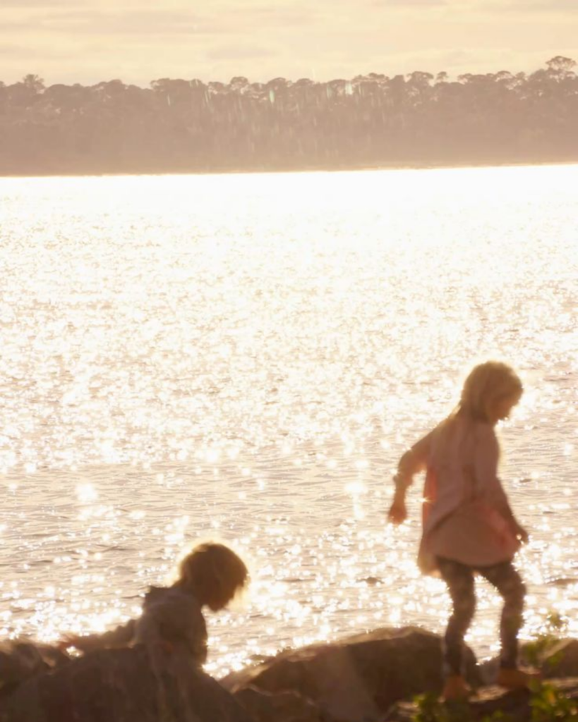 Two children playing on the rocks by sparkling water at sunset
