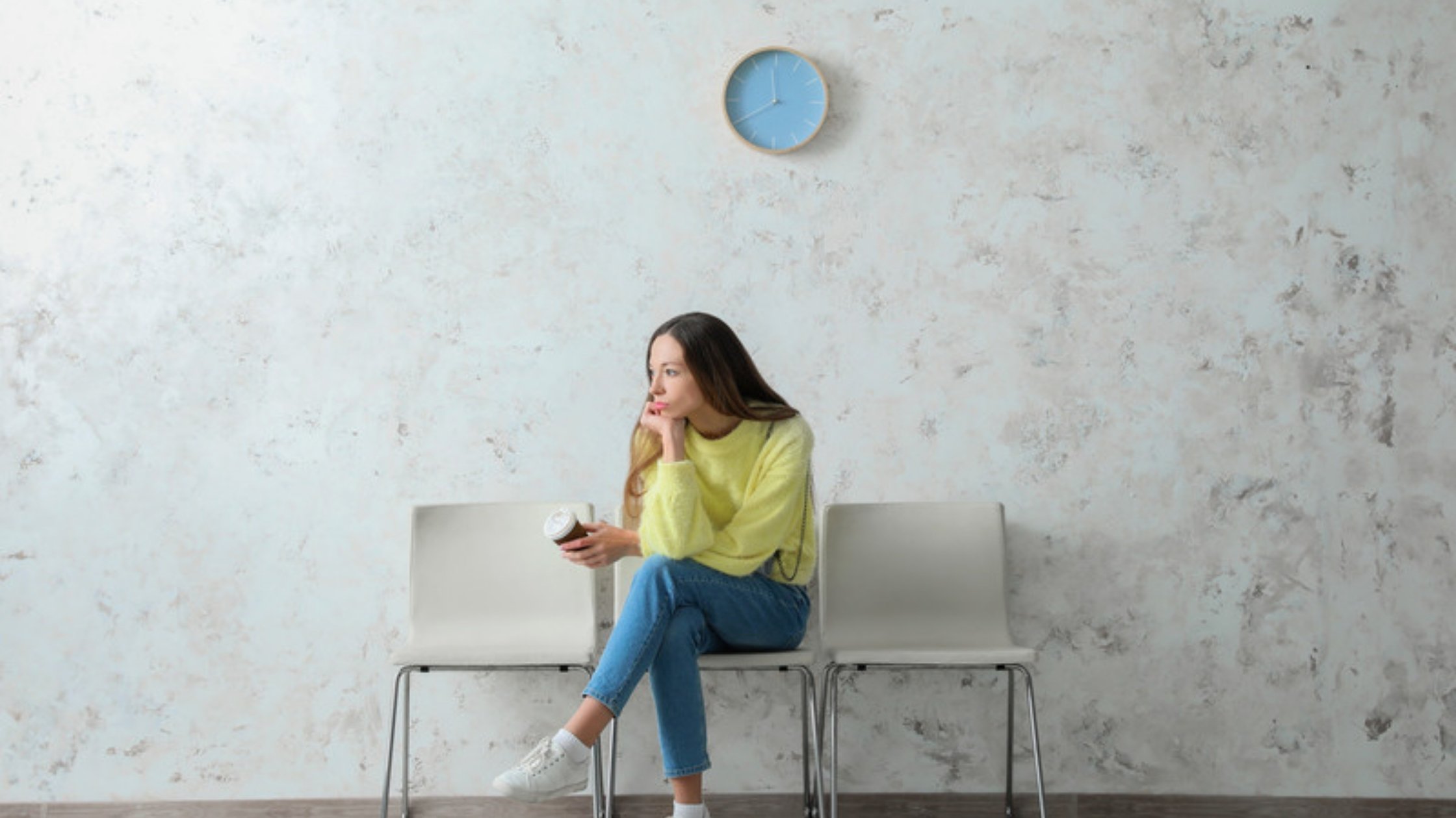 Woman sitting alone in a waiting room under a clock, waiting anxiously