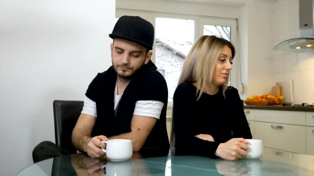 Couple sitting apart at a kitchen table, avoiding eye contact