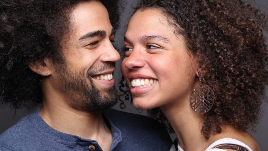 Smiling couple with curly hair standing cheek to cheek