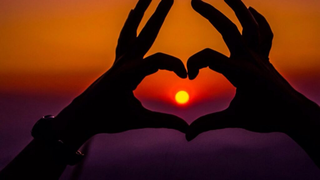 Hands making a heart shape around the setting sun