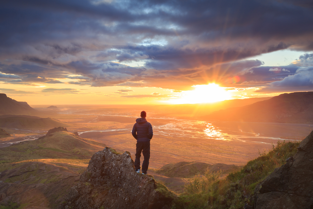 Person standing on a mountain looking out at the sunset
