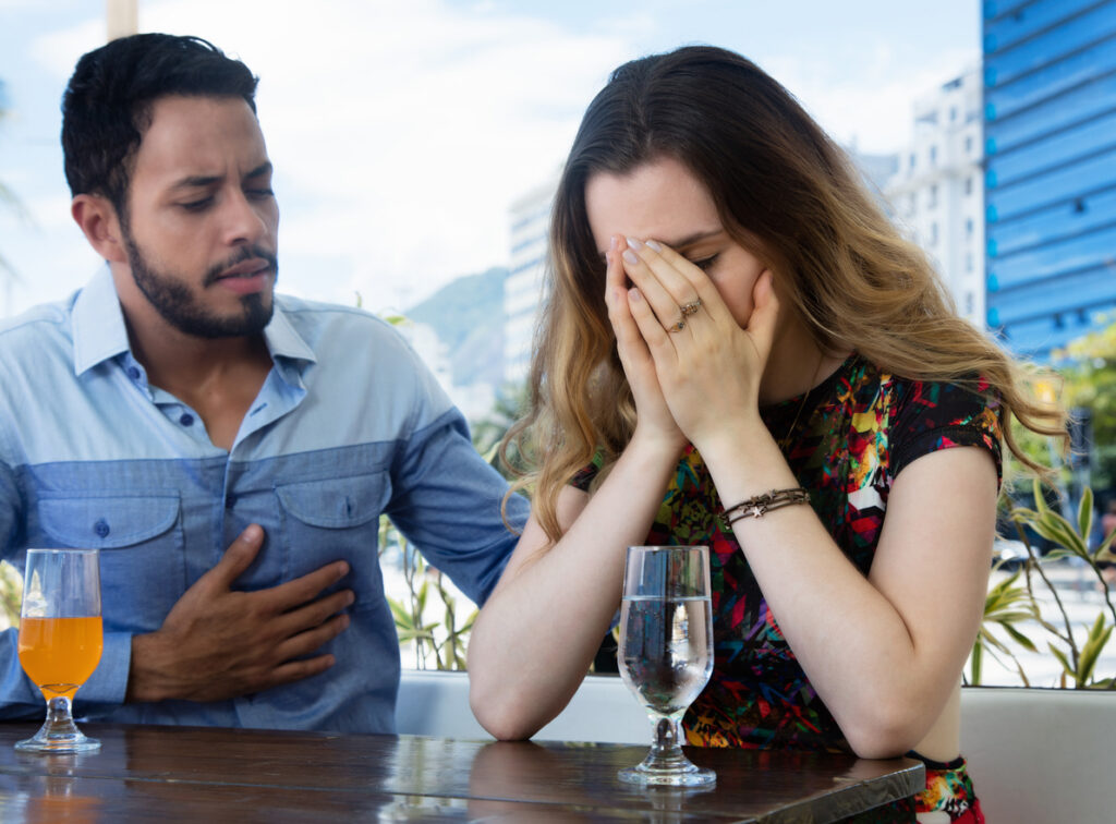 Woman covering her face in frustration while her partner sits beside her