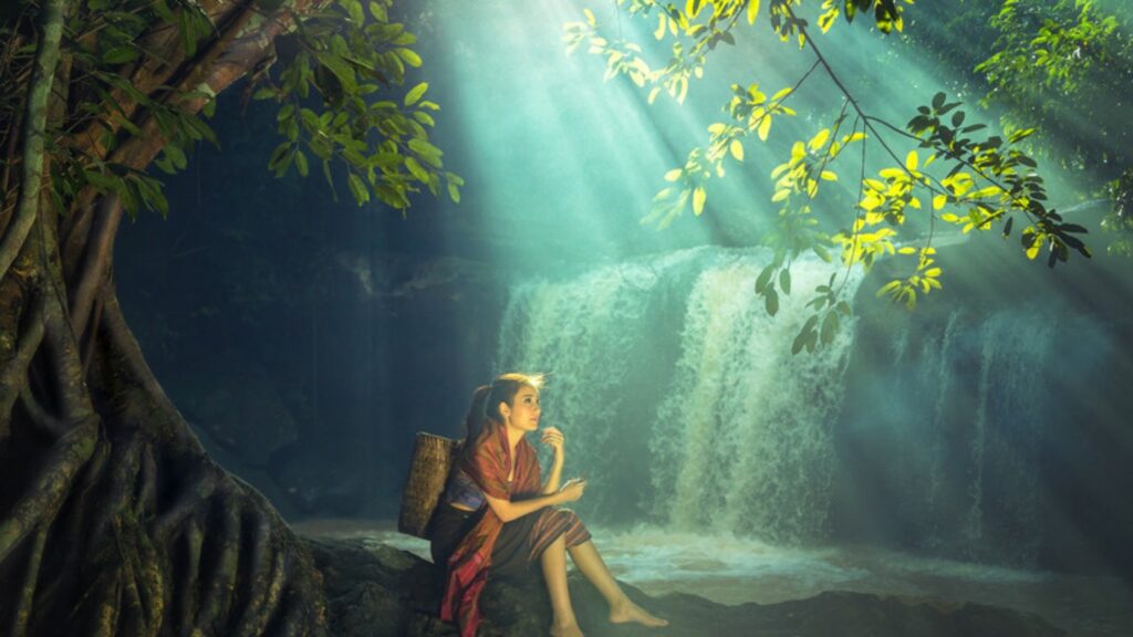 Woman sitting by a waterfall in a beam of forest light