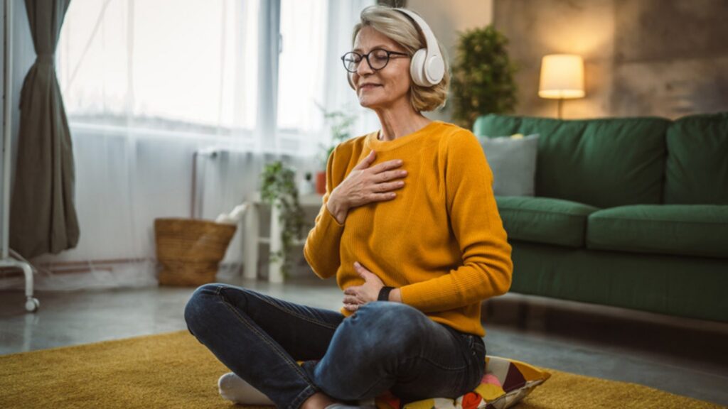 Woman sitting on the floor with headphones and a hand on her heart, resourcing herself